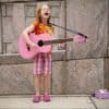 Girl having fun playing pink guitar. Busking outside.