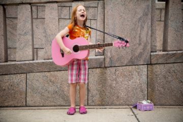 Girl having fun playing pink guitar. Busking outside.