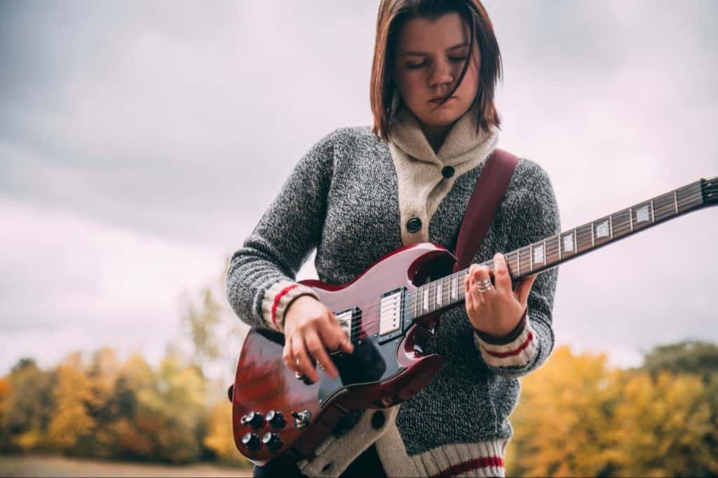 Girl maxing out on guitar. Playing red guitar.