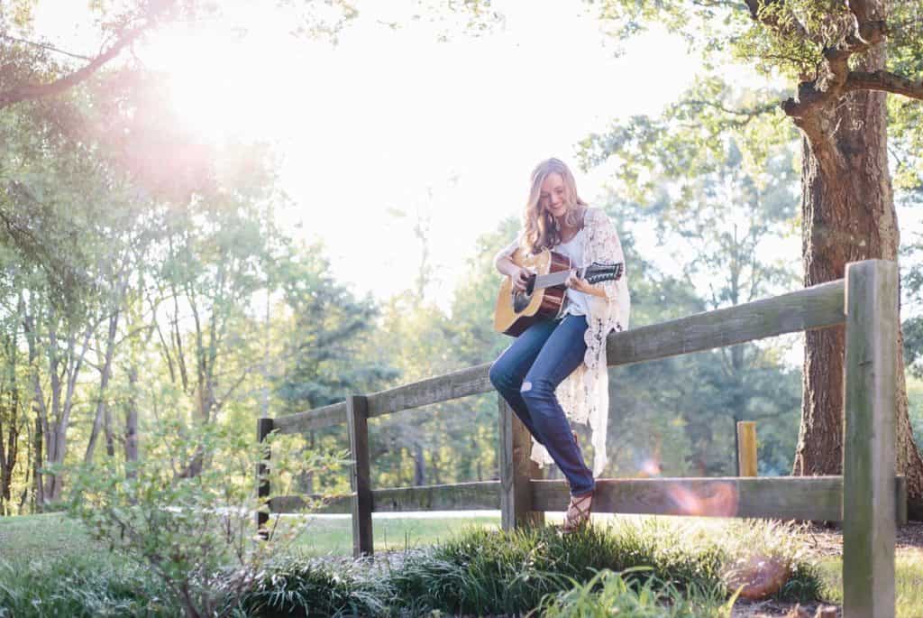 Woman playing guitar outside on fence, having fun.