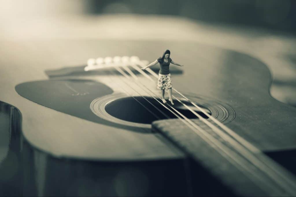 Girl walking on guitar strings, balancing on a BUILDING size guitar.