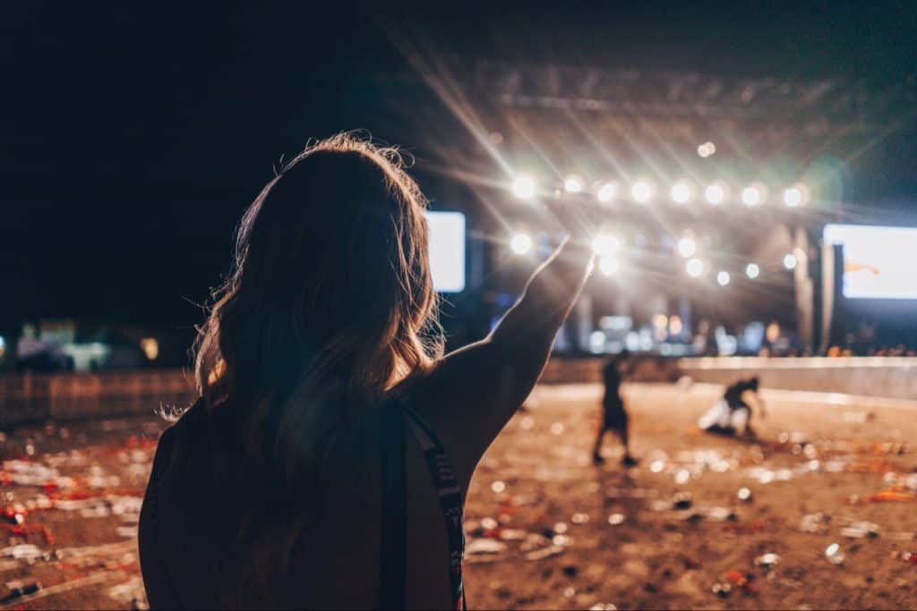 Girl waving hand toward a concert stage. People in background, picking up litter.