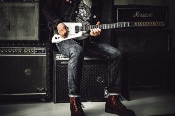 Man in jeans playing guitar on top of amplifier