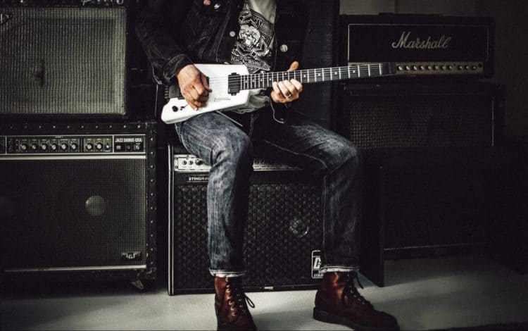 Man in jeans playing guitar on top of amplifier