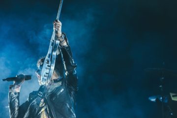 Man holding guitar up, with microphone in the other hand.