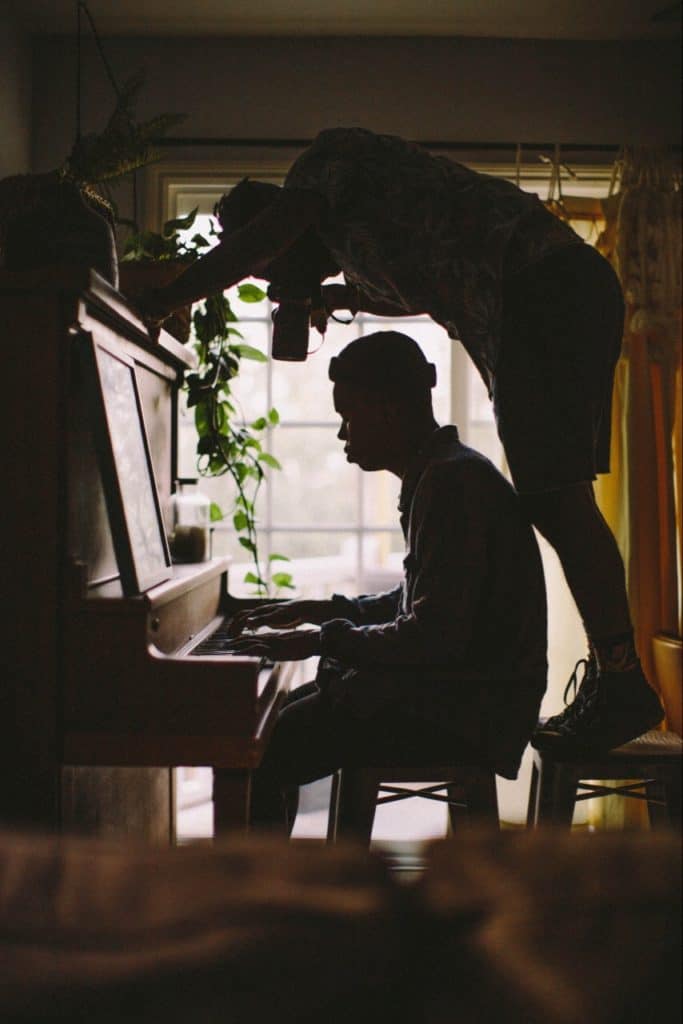 Camera man filming piano player on top of chair, behind him.