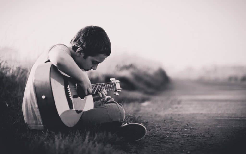 Little kid playing guitar in field beside country road.