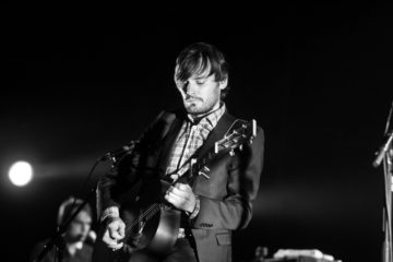 Man playing guitar on stage confidently. Black and white picture.