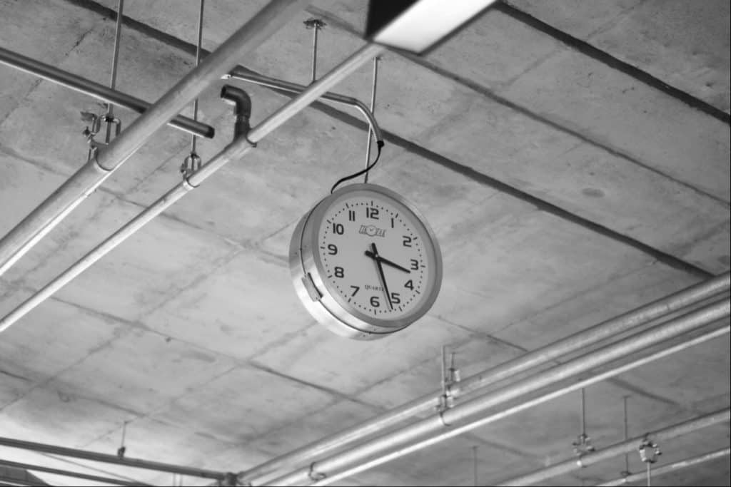 Silver Clock hanging from ceiling, in a room.