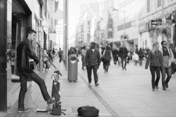 Doing good busking outside, having fun playing guitar. Black and white photo.