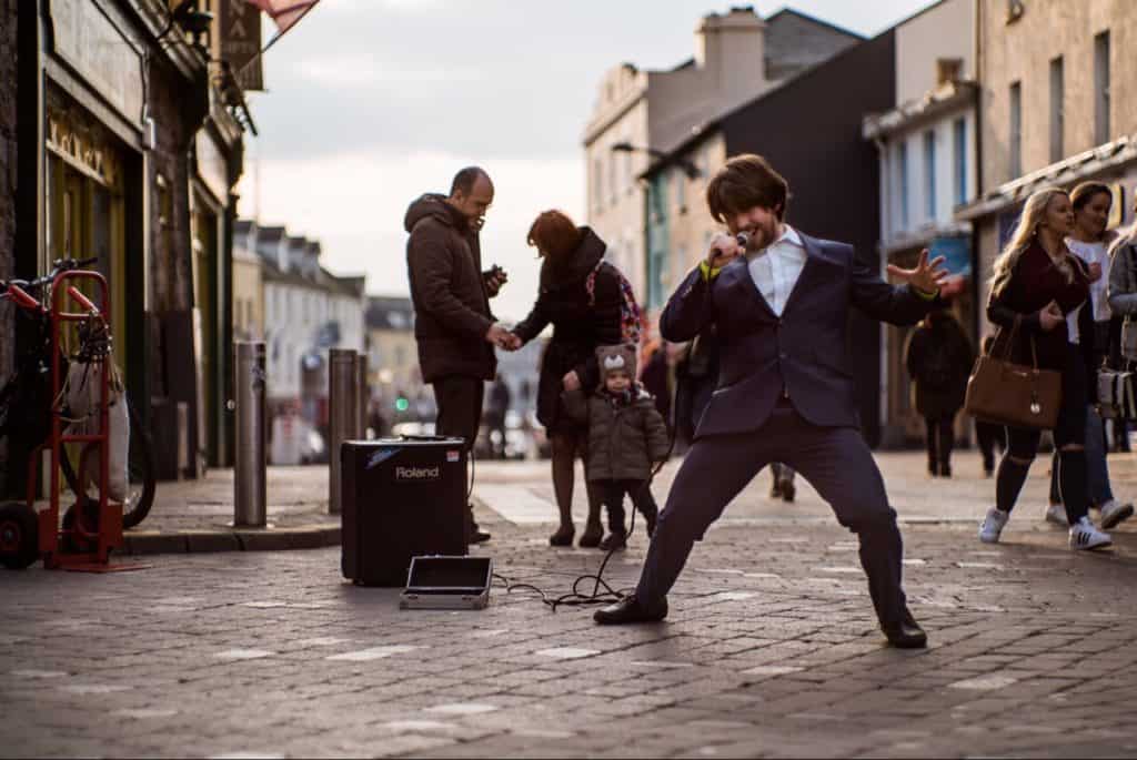 Man having all kinds of fun singing in the street with microphone in hand.