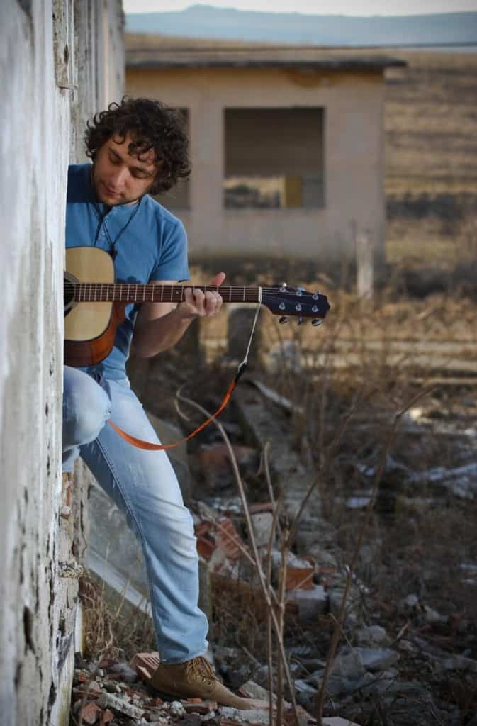 Man playing guitar halfway out of building, having fun.