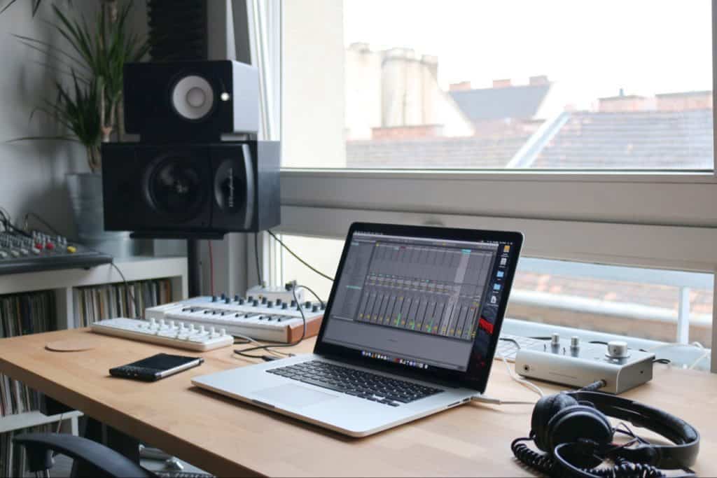 Laptop used for music. Music keyboard and headphones and cellphone. And speakers hanging on wall.