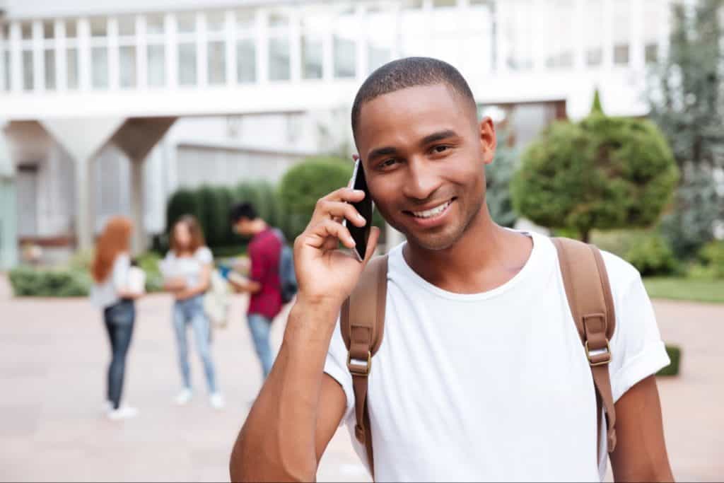 Cool young man making phone call outside. Behind him are young people.