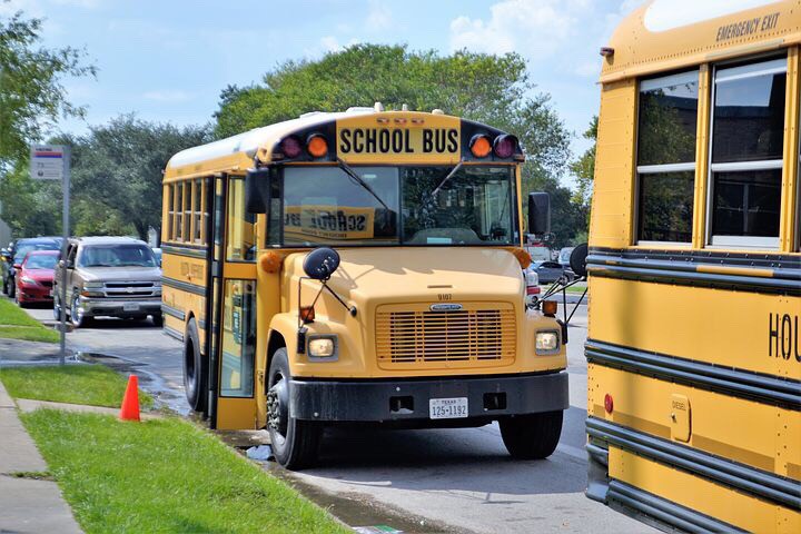 Two bright yellow school buses parked in front of school. Photo courtesy of ArtisticOperations. Photo found on pixabay.com