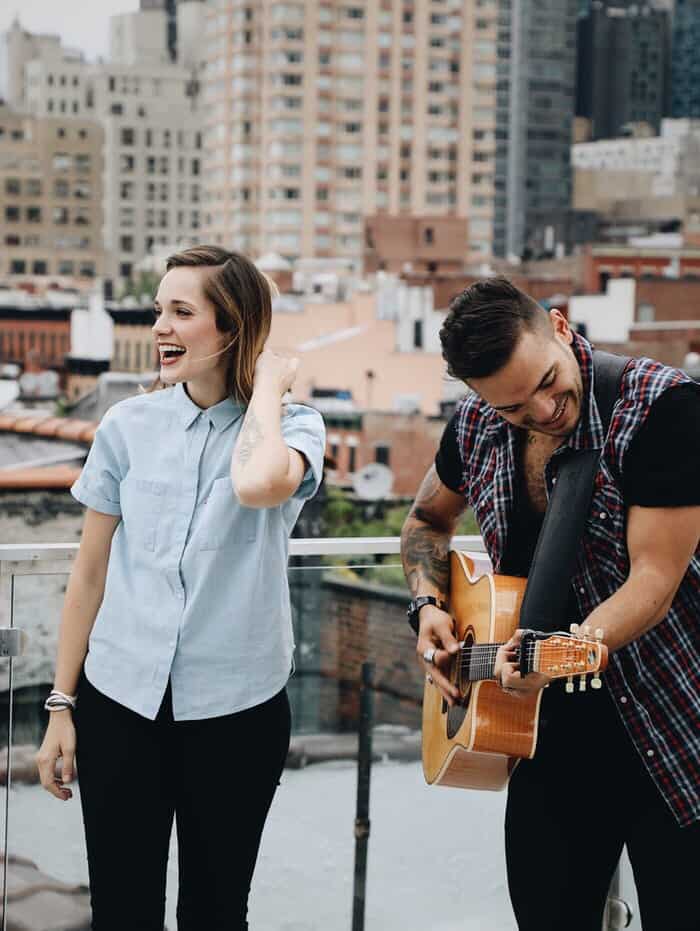 Young man and woman outside, with him on guitar jamming and her singing.