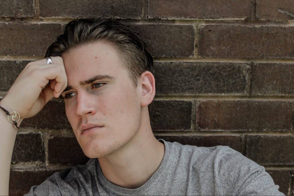 Young man thinking against brick wall, outside.