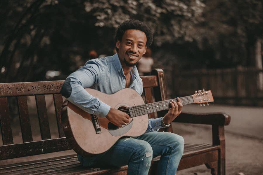 Man playing acoustic guitar outside, having fun playing it and smiling.