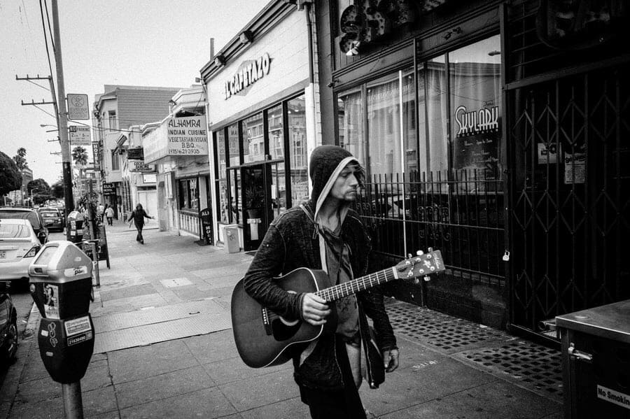 Man going into store with acoustic guitar.