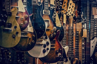 Lots of various guitars hanging up on the side of wall, inside of store.