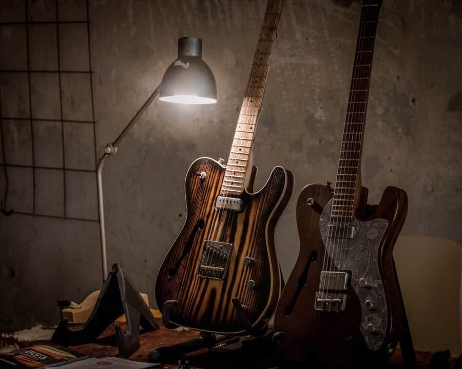 Two guitars side by side, with lights shining down on one of them.