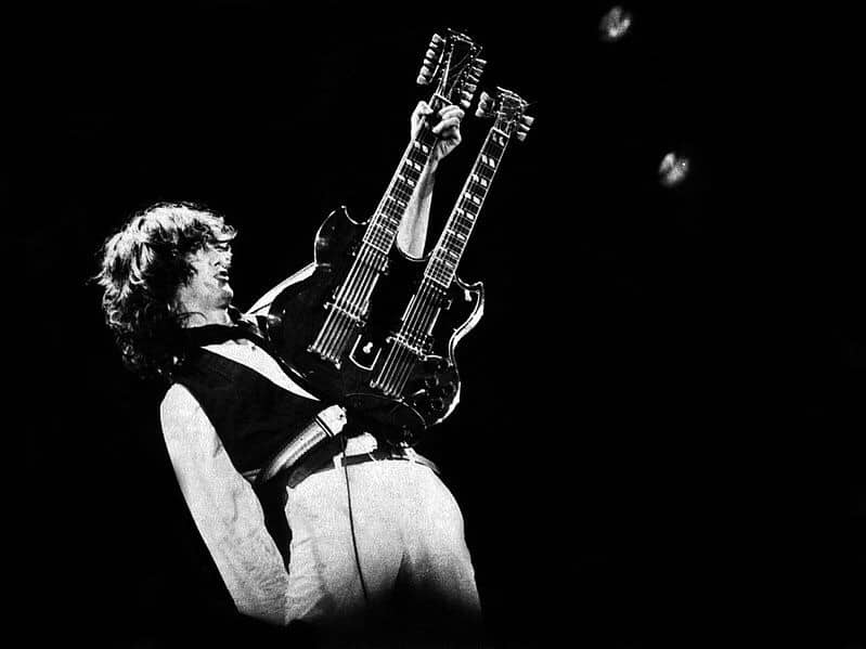 Jimmy Page holding double guitar up, real high in the air, looking cool.