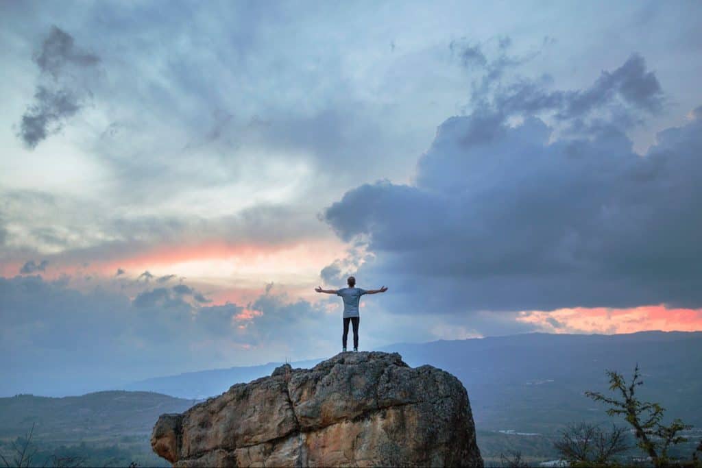 Man on top of high boulder mountain, very excited, with hands extended.