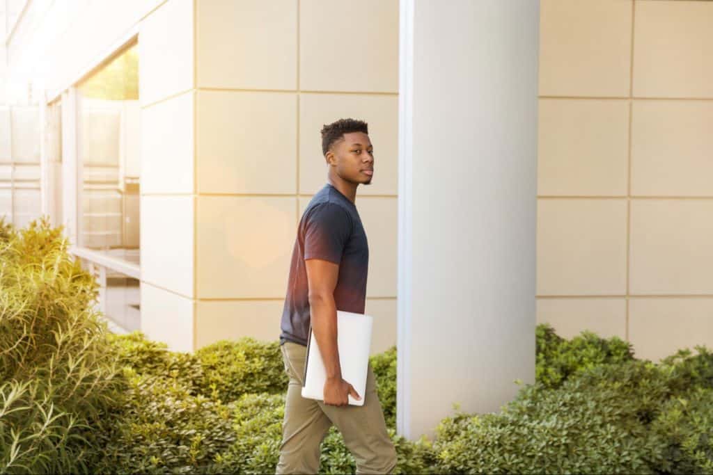 Young man going into a building, with a laptop.