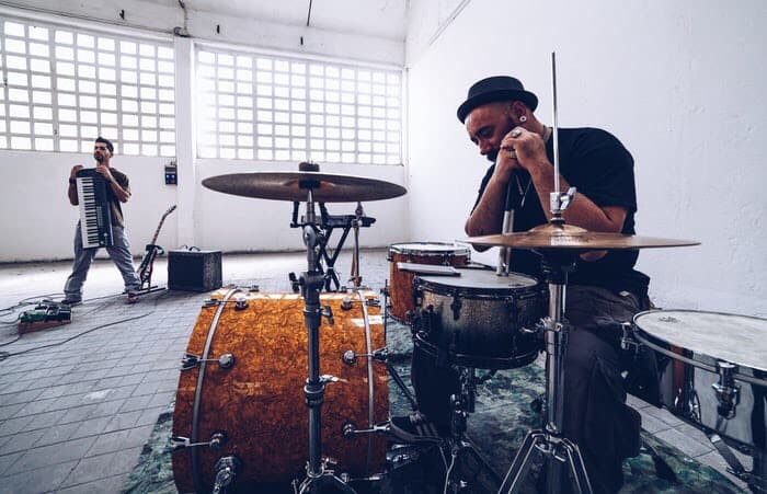 Drummer reading on drums. And keyboard player holding keyboard up in his arms. Inside big building.