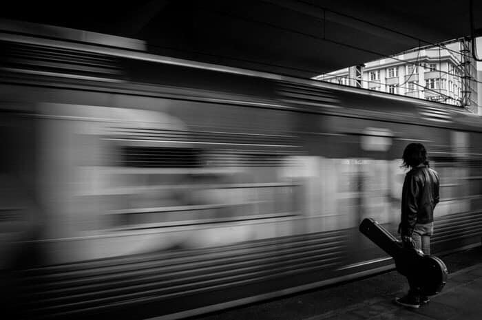 Man with guitar standing very, very, close to fast moving train. Black and white picture.