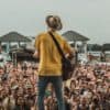 Man on tall stage, playing guitar before huge crowd, pleasing them with his playing. Image from unsplash.com