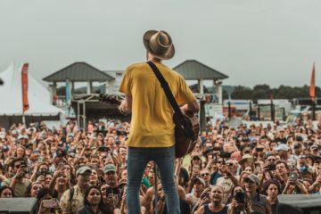 Man on tall stage, playing guitar before huge crowd, pleasing them with his playing. Image from unsplash.com