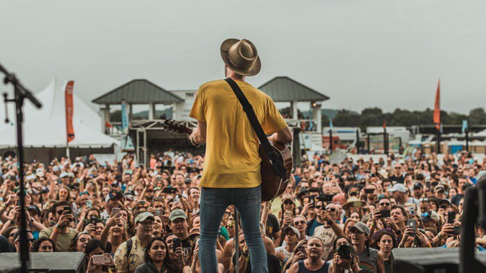 Man on tall stage, playing guitar before huge crowd, pleasing them with his playing. Image from unsplash.com