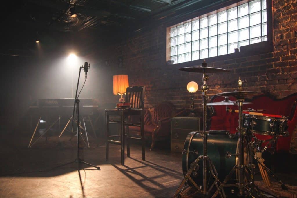 Drums and keyboard and microphone and a high chair, all in a big beautiful room.