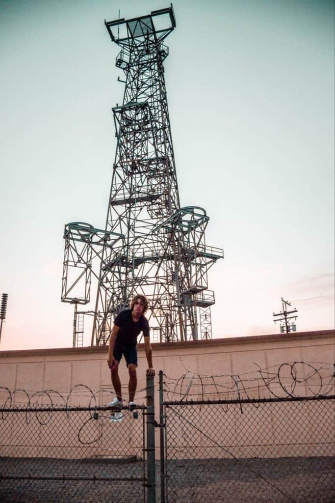 Gigantic antenna and kid climbing on the barbed wire fence in front of it.