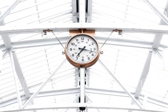 Gold clock hanging from bars in big sun roof building.