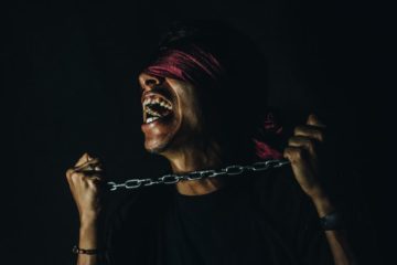 Man going crazy, has chain to his neck and blindfold covering his eyes.