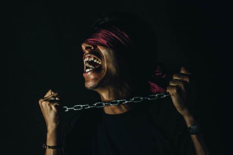 Man going crazy, has chain to his neck and blindfold covering his eyes.