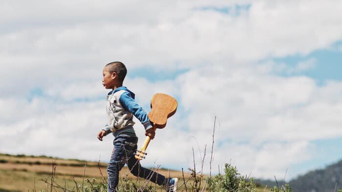 Kid running with ukulele in field.