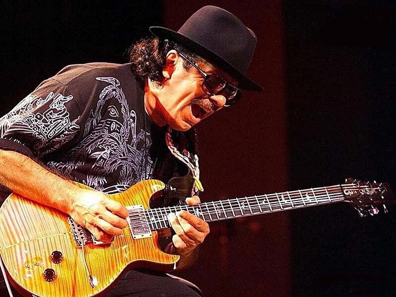 Carlos Santana getting off on playing and bending strings on guitar, on stage.