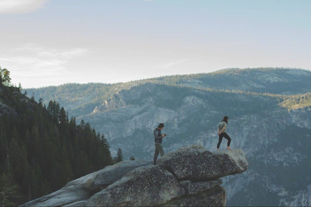 Young man and woman on top of mountain with woman in front, looking down.