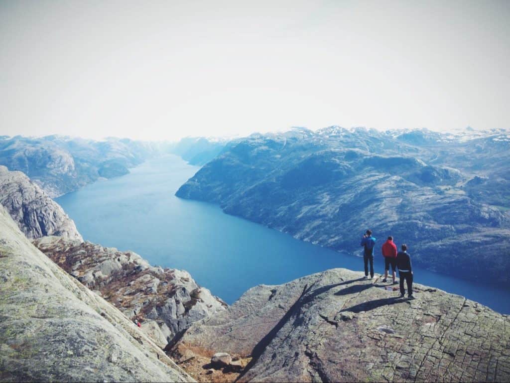 Three people on top of mountain looking outward at the scenery before them.