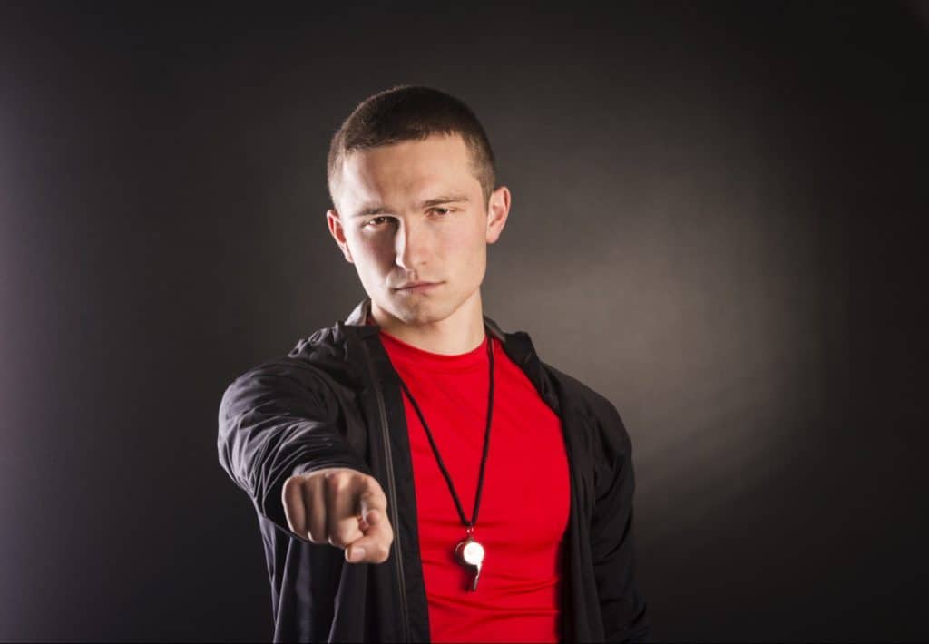 Man with whistle, pointing, looking firm.