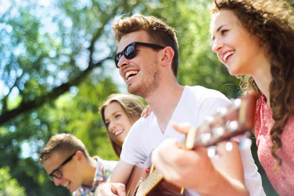 Young man enjoying playing guitar outside, with others. Image from storyblocks.com