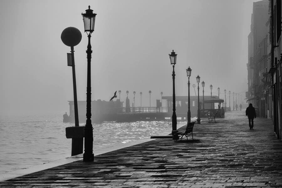 Man walking on the dreary street next to the ocean. Dreary and misty, and humid picture. Black and white picture.