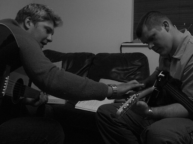 Man showing another man how to play something on the guitar. Photo courtesy of JamieMBrown from flickr.com