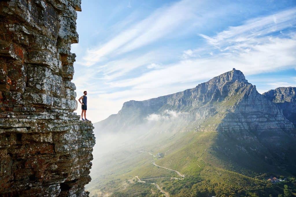 Man standing on a cliff, extremely high up on a mountain, real beautiful view below and all around.