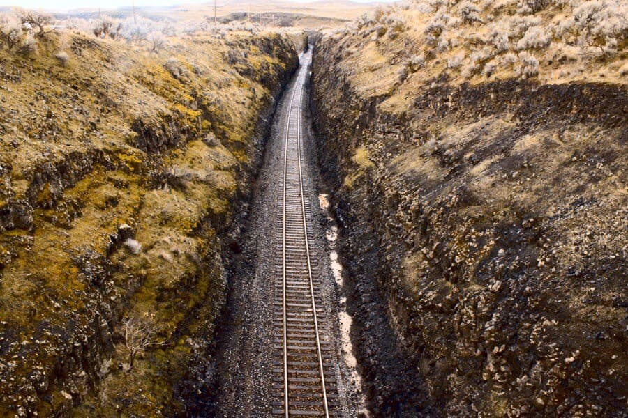 Railroad tracks alongside big green mountains, on both sides of it.