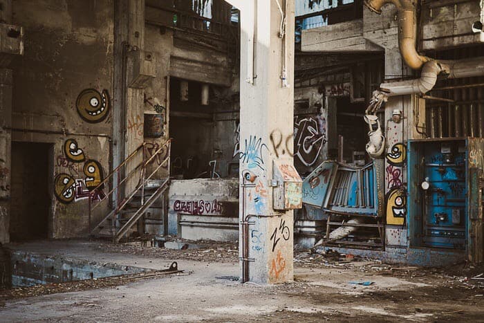 Graffiti filled building, with post in it and also a square hole in the floor.