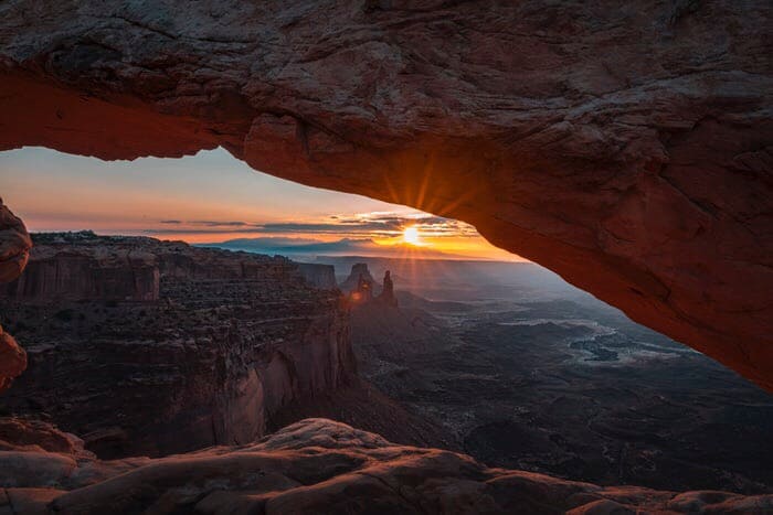 A bouldered cave with a opening, showing the glorious sun and bouldered rock mountains, out of the opening.